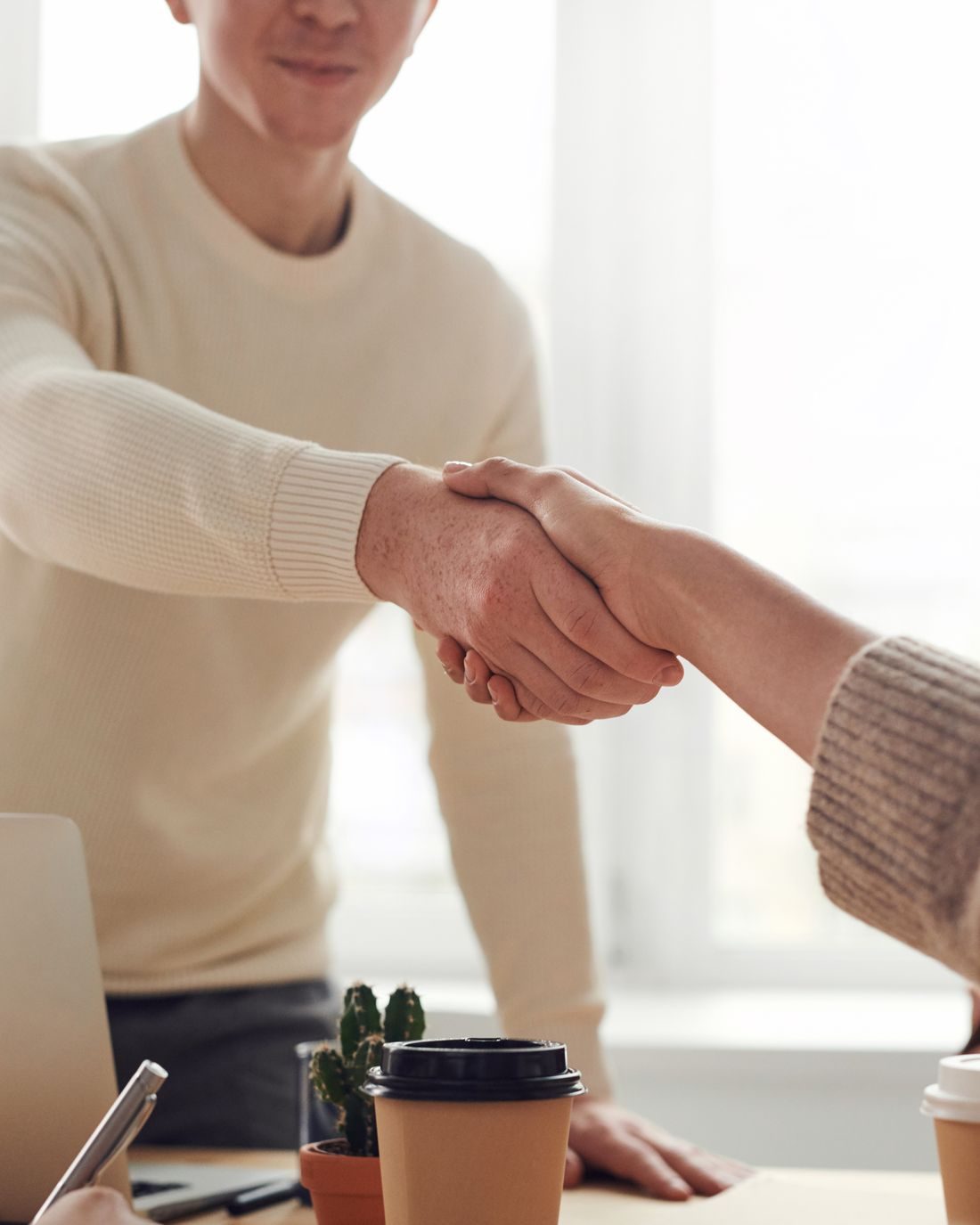Dos personas cerrando un acuerdo con un apretón de manos sobre un escritorio